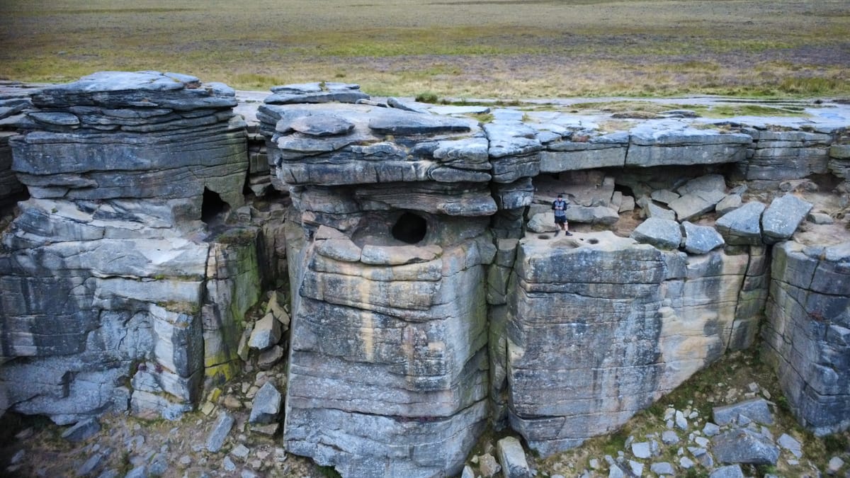 Robin Hood’s Cave at Stanage Edge, showing weathered cliffs with a person standing at the entrance.